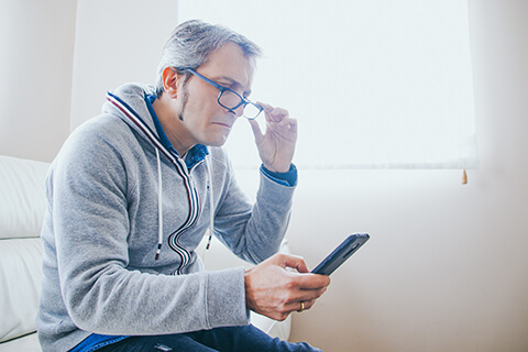 Man who needs reading glasses so see mobile phone